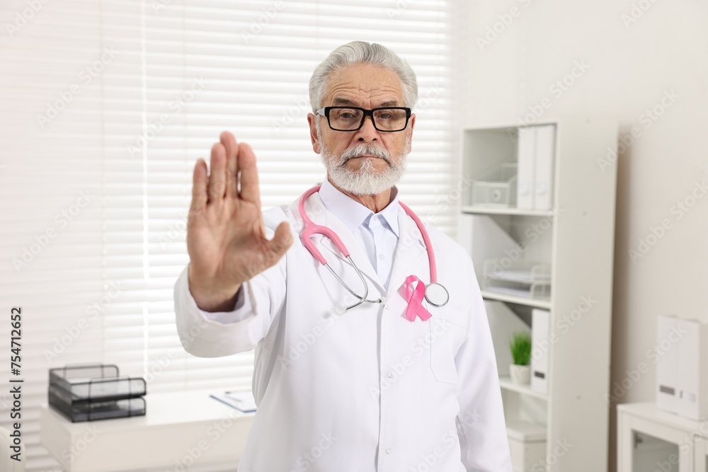 Mammologist with pink ribbon showing stop gesture in hospital. Breast cancer awareness Mammologist with pink ribbon showing stop gesture in hospital. Breast cancer awareness