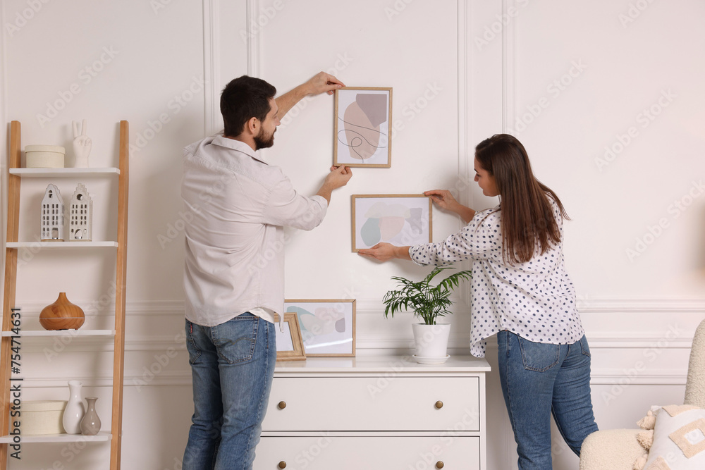 Man and woman hanging picture frames on white wall at home Man and woman hanging picture frames on white wall at home
