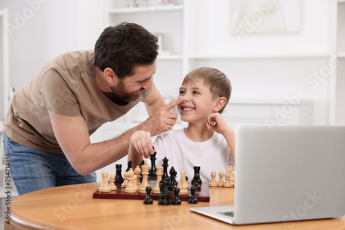 Father teaching his son to play chess following online lesson at home