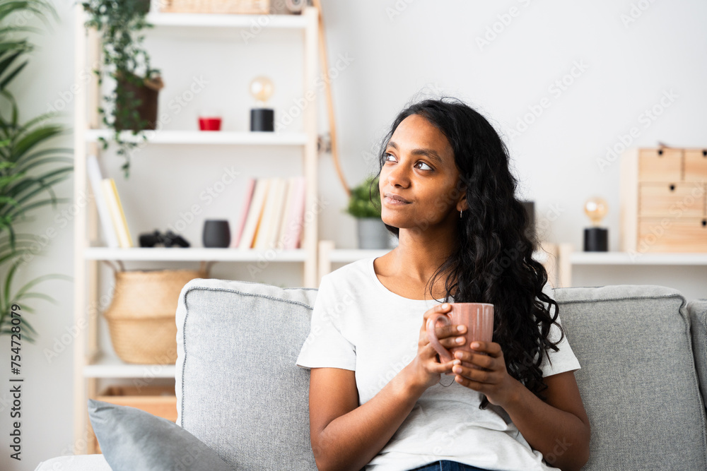 Pensive Indian woman holding cup of coffee at home Pensive Indian woman holding cup of coffee at home
