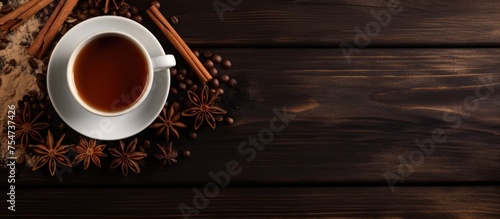 A top view of a wooden table featuring a cup filled with tea surrounded by aromatic cinnamon sticks and star anise. The warm beverage emits a comforting scent, creating a cozy atmosphere.