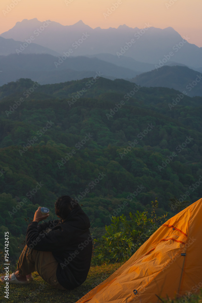 Fototapeta premium nature traveling with orange camping tent and layer of mountain with solo man drink coffee and see sunrise