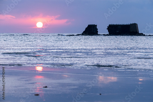 Alba sul mare con riflesso del sole sulla sull'acqua e sulla sabbia.