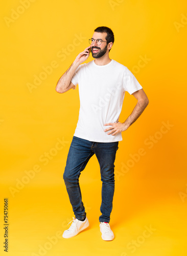 Full-length shot of man with beard over isolated yellow background keeping a conversation with the mobile phone