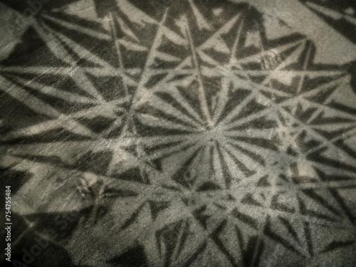 暗い砂地背景に複雑な古いゴシック様式の幾何学文様の影が投影されたイメージアート