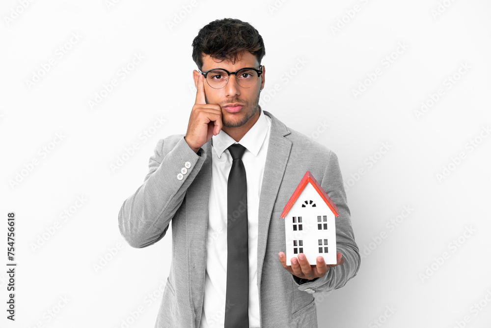 Business man holding a house isolated on blue background thinking an idea Business man holding a house isolated on blue background thinking an idea