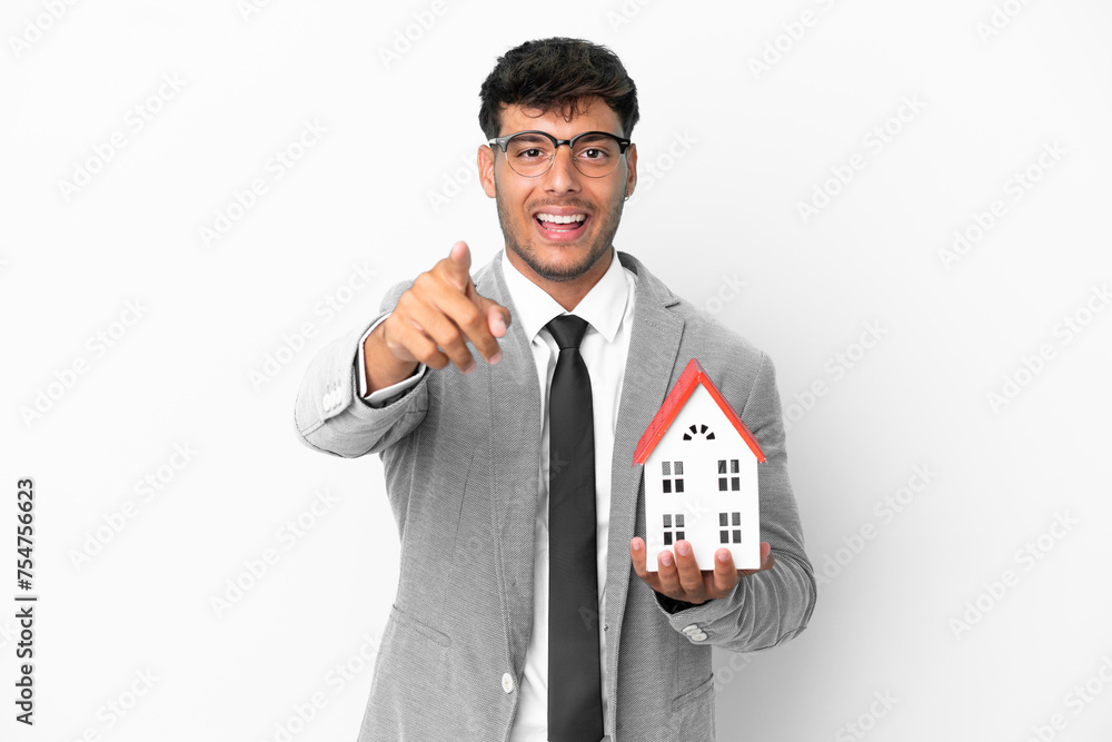 Business man holding a house isolated on blue background surprised and pointing front Business man holding a house isolated on blue background surprised and pointing front
