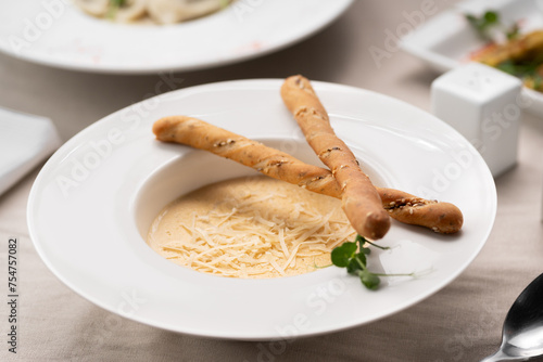 Hot creamy potato soup with cheese served on a white plate with bread sticks. Vegetarian food