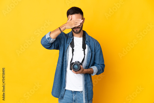 Young photographer girl isolated on yellow background covering eyes by hands. Do not want to see something © luismolinero