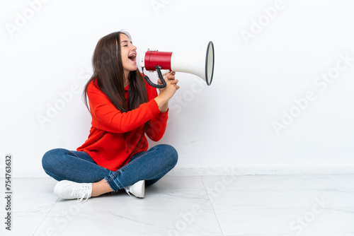 Young Ukrainian woman sitting on the floor isolated on white background shouting through a megaphone