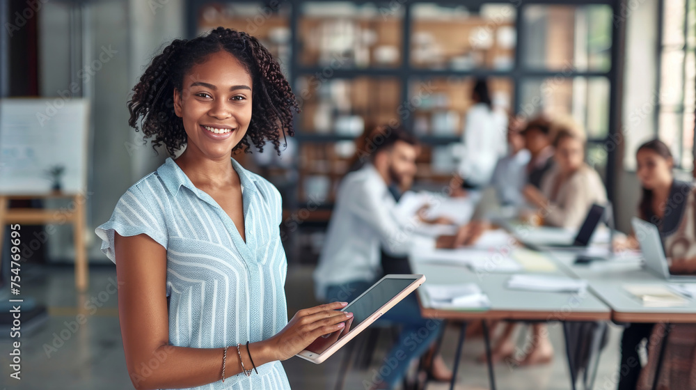 Smiling Young African American Woman Holding Tablet with Colleagues Working in Background Smiling Young African American Woman Holding Tablet with Colleagues Working in Background