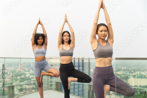 Young Asian woman and African American exercise yoga on the rooftop.Group of happy fit friends exercising outdoor in city.