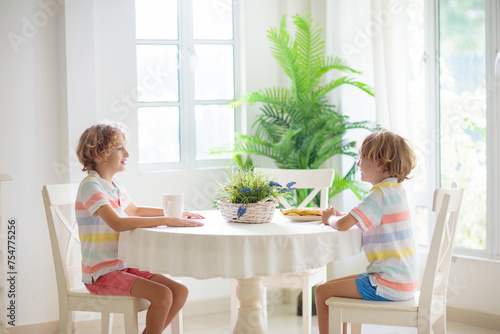 Kids eating breakfast in white kitchen.