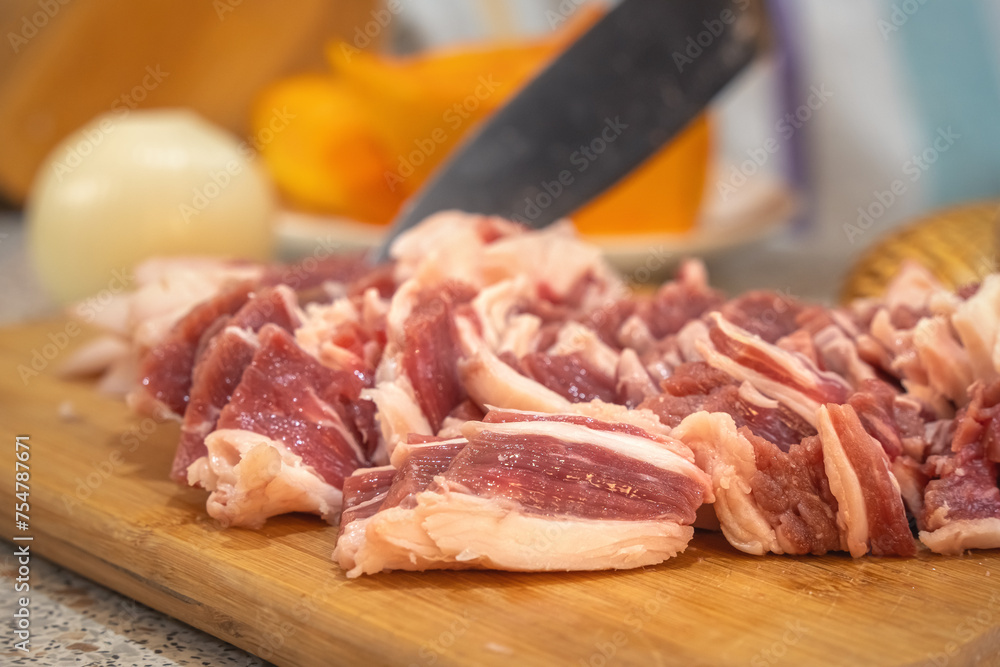 Beautifully cut slices of fresh fatty meat for further cooking on a background of bamboo utensils and vegetables. Close-up