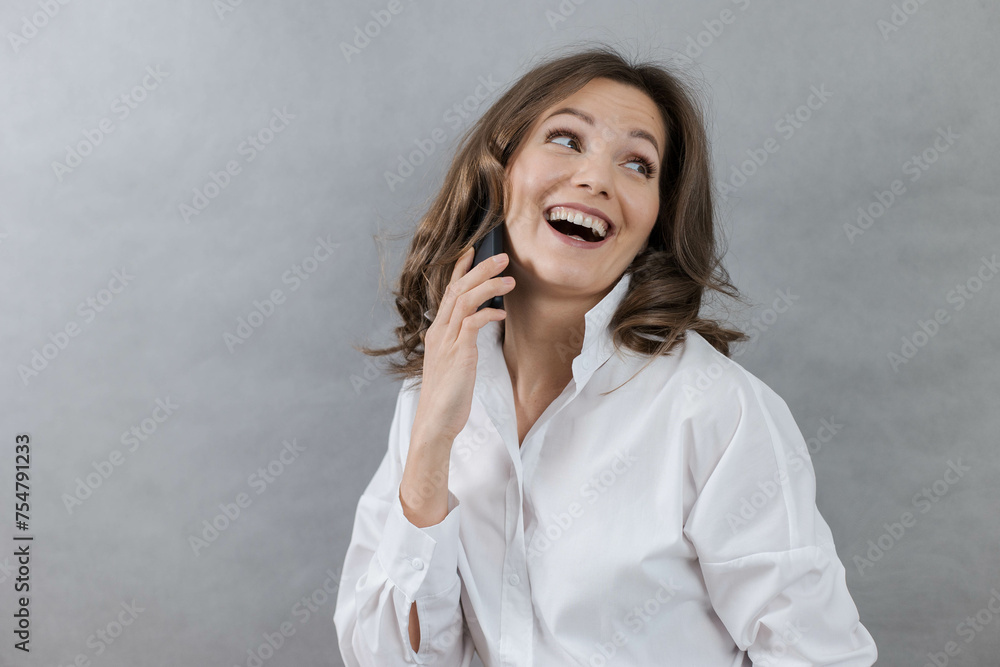 Young woman smiling happily while talking on smartphone on grey background, copy space. Young woman smiling happily while talking on smartphone on grey background, copy space.