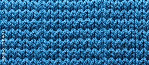 A detailed view of a blue knitted material, showcasing the textured background created by hand knitting with facial loops. The intricate patterns and stitches are visible up close.