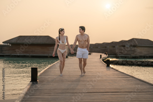 Couple walking on wooden bridge by the beach during sunset. photo
