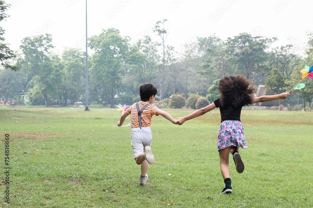 Cheerful two little kids having fun while running in park. Boy and girl running around holding a windmill. Children having fun, with happy smile. Best friends concept.