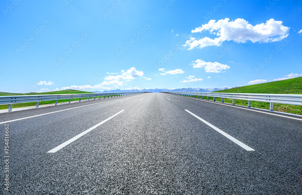 Fototapeta premium Straight asphalt road and green meadow with mountain nature landscape under blue sky