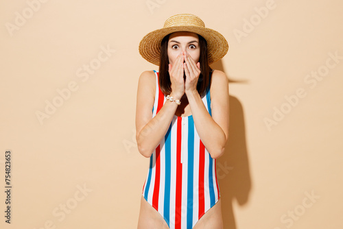 Young impressed excited sexy woman wears one-piece swimsuit straw hat near hotel pool cover mouth with hand isolated on plain pastel light beige background. Summer vacation sea rest sun tan concept.