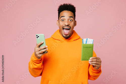 Traveler man wear yellow casual clothes hold passport ticket use mobile cell phone isolated on plain pink background. Tourist travel abroad in free time rest getaway. Air flight trip journey concept.