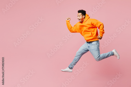 Full body side profile view fun young man of African American ethnicity he wear yellow hoody casual clothes jump high run fact isolated on plain pastel light pink background studio. Lifestyle concept.