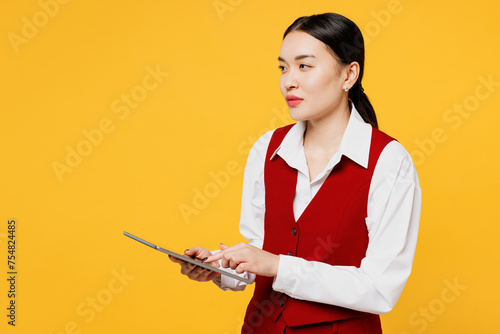 Young smart corporate lawyer employee business woman of Asian ethnicity wears formal red vest shirt work at office use digital tablet pc computer isolated on plain yellow background. Career concept.