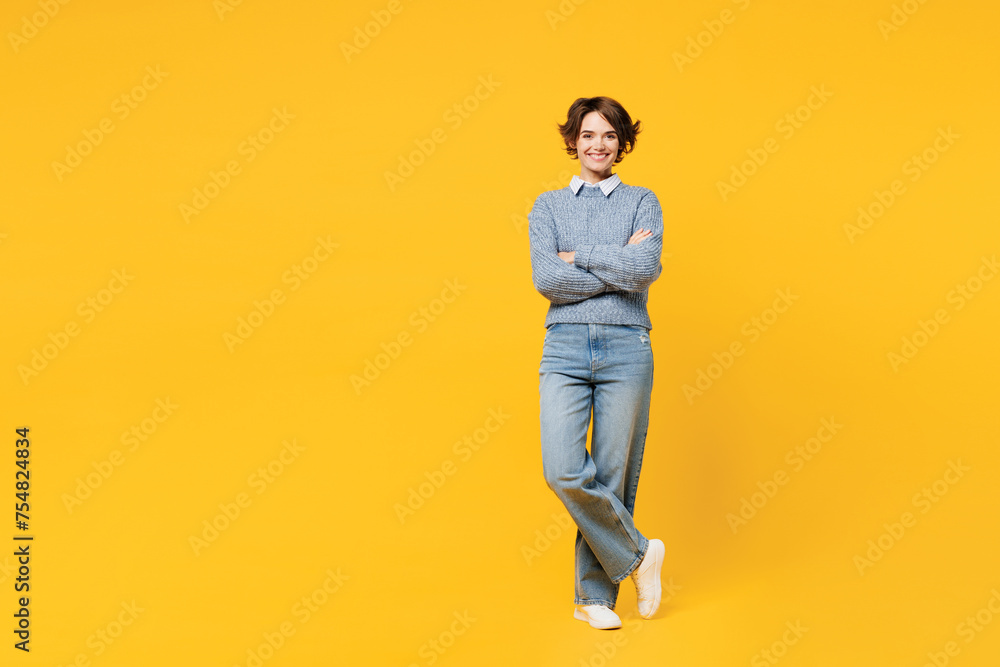 Full body smiling happy young woman wears grey knitted sweater shirt casual clothes stand hold hands crossed folded look camera isolated on plain yellow background studio portrait. Lifestyle concept. Full body smiling happy young woman wears grey knitted sweater shirt casual clothes stand hold hands crossed folded look camera isolated on plain yellow background studio portrait. Lifestyle concept.