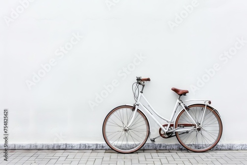 White vintage bicycle with brown leather saddle leaning against a white wall on a tiled sidewalk