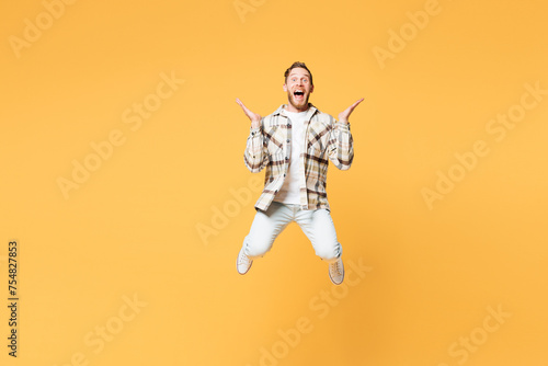 Full body overjoyed exultant young Caucasian man wear brown shirt casual clothes jump high spread hands scream look camera isolated on plain yellow orange background studio portrait Lifestyle concept