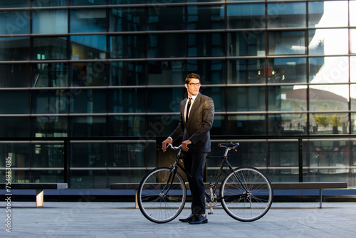 Handsome young business man wearing elegant corporate suit going to work with bicycle, concepts of transportation, green mobility and eco friendly lifestyle