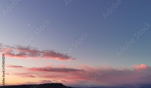 La Luna all   alba resta ancora nel cielo sopra le nuvole rosa sulla colline mentre il sole sorge dal mare