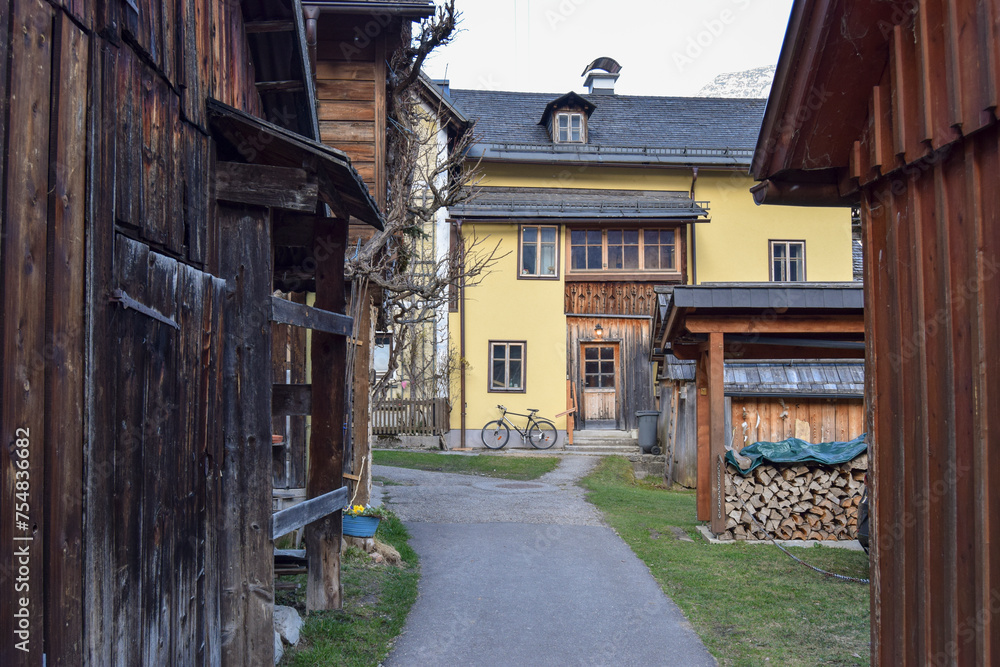 Fototapeta premium Callejuela rural con casas de madera a los lados y una casa amarilla al fondo con una bicicleta