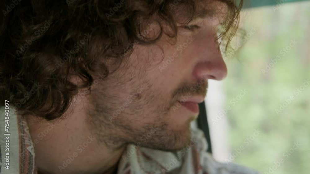 Close-up of young unshaven man in shirt looking forwards while sitting inside camper van and moving to countryside while traveling on summer weekend on his own Close-up of young unshaven man in shirt looking forwards while sitting inside camper van and moving to countryside while traveling on summer weekend on his own