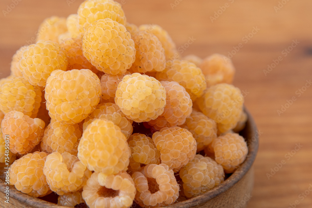 Yellow raspberries in a wooden bowl on the table. Summer berries background. Vitamin food, berry harvest. Healthy nutrition. Yellow raspberries in a wooden bowl on the table. Summer berries background. Vitamin food, berry harvest. Healthy nutrition.