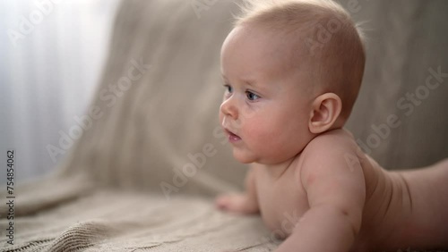 Closeup of cute little baby girl lying on stomach on bed, learning to hold head. Portrait of nice newborn naked baby looking interestingly away. Carefree healthy babyhood, healthcare concept. photo