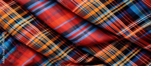 A close-up view of a Scottish tartan fabric featuring vibrant red, blue, and yellow colors in a classic check pattern. The loops and abstract texture create a retro decorative design on the cloth.