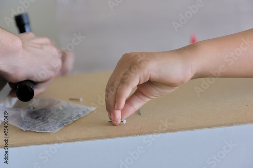 A child actively participates, observes, and learns alongside an adult while assembling new furniture in their home. Symbolizes the transfer of experience to the younger generation and the shared work