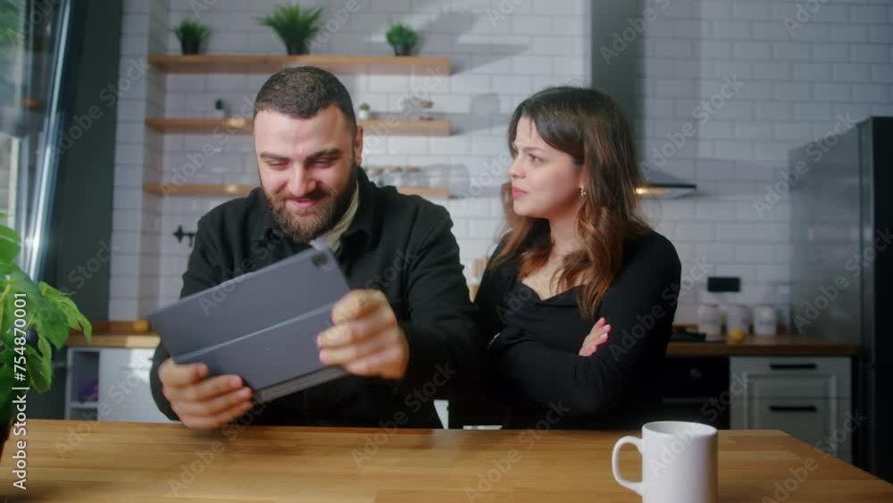 Young lovers sitting in the kitchen, man playing a racing mobile game on tablet computer woman messing with the her boyfriend Young lovers sitting in the kitchen, man playing a racing mobile game on tablet computer woman messing with the her boyfriend