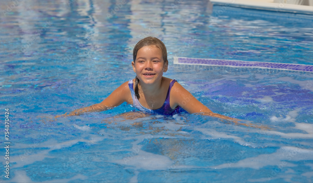 A joyful child happily swimming and enjoying leisure time in an open pool with clear blue water. Active summer recreation in a resort with a swimming pool, embodying the essence of a happy childhood.
