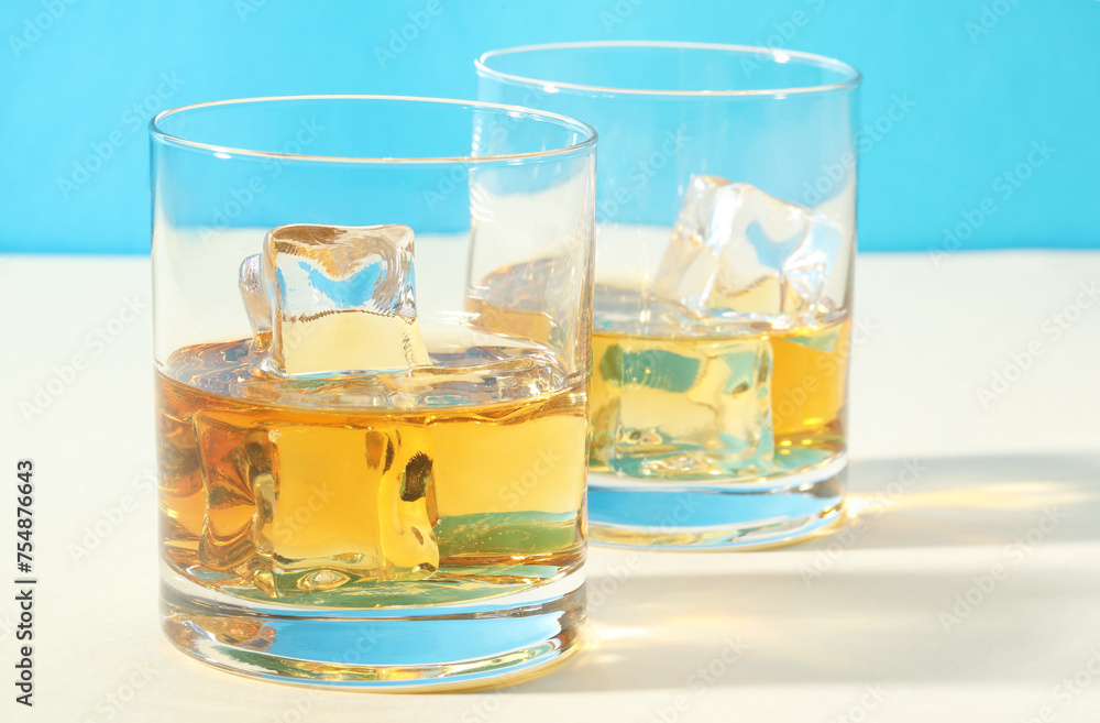 Whiskey with ice cubes in glasses on white table, closeup Whiskey with ice cubes in glasses on white table, closeup