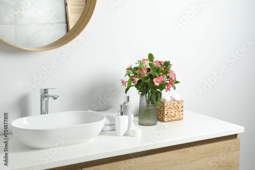 Vase with beautiful Alstroemeria flowers and toiletries near sink in bathroom