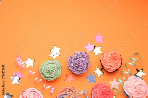 Delicious cupcakes with bright cream and party decor on orange background, flat lay. Space for text