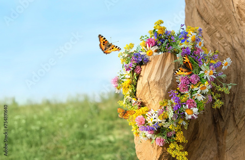 butterflies and colorful flowers wreath on tree on meadow. summer background. Floral crown, symbol of Summer Solstice Day, Midsummer holiday, Litha sabbat. witch, wiccan ritual. copy space