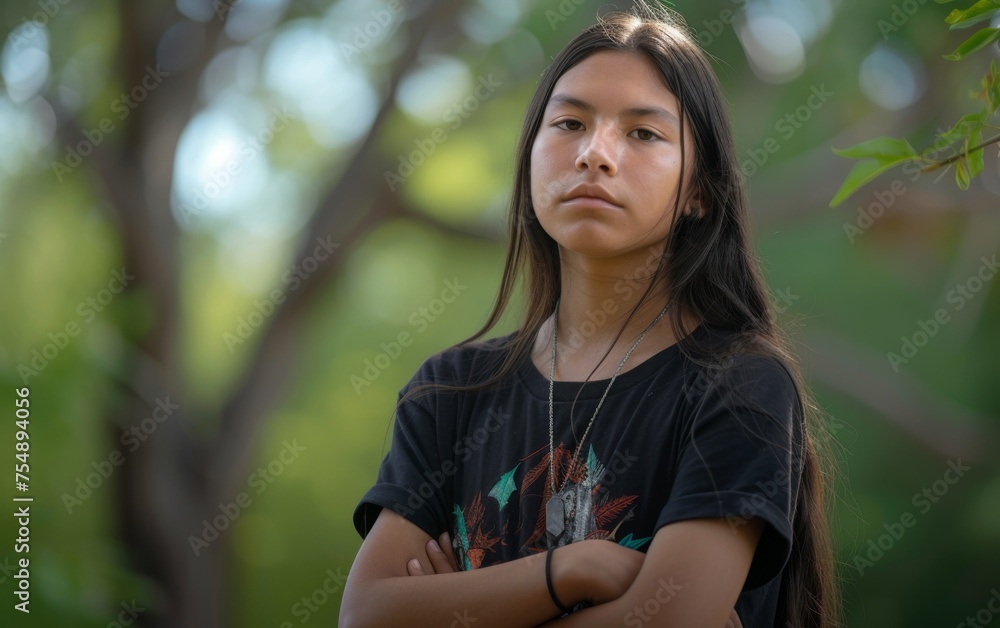 A young woman with long hair is standing in a park, wearing a black shirt and a necklace. She is looking at the camera with a serious expression