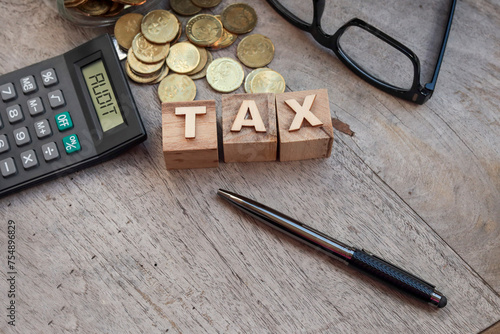 Wooden cubes with the TAX. A pile of coins, a calculator, and eyeglasses at the back. Business and audit tax concept