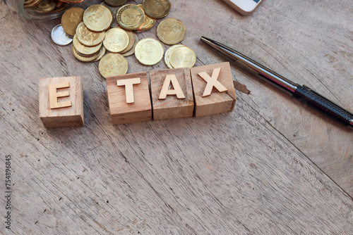 Business and e-tax concept. The word E TAX is written on the wooden cubes. A pile of coins, pen, and smartphone at the background