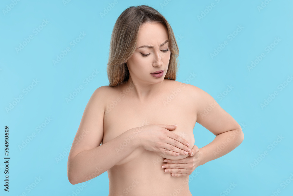 Fototapeta premium Mammology. Naked young woman doing breast self-examination on light blue background