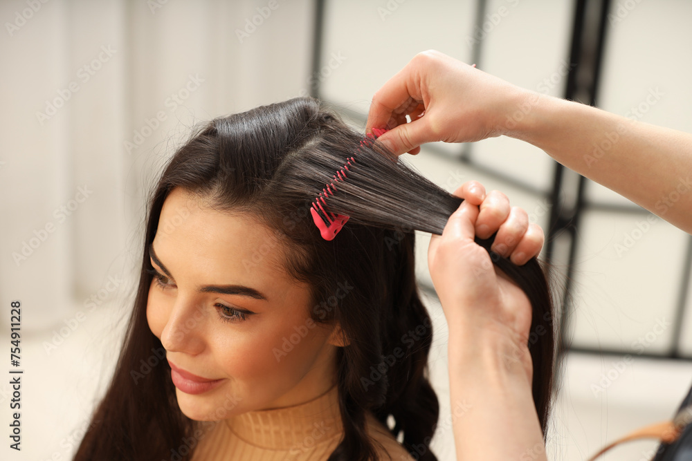 Fototapeta premium Hair styling. Professional hairdresser combing woman's hair indoors, closeup