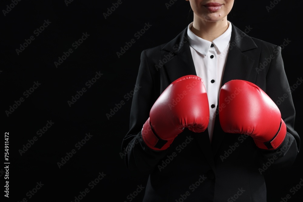 Businesswoman in suit wearing boxing gloves on black background, closeup. Space for text
